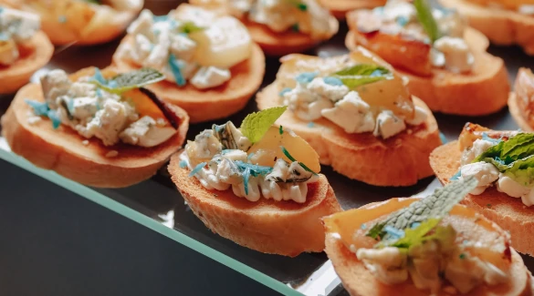 Assortiment de canapés frais avec fromage, fruits et menthe sur toasts, parfaits pour les menus buffets de Gustus...