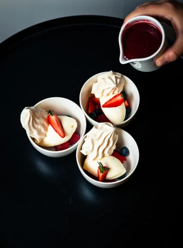 Desserts individuels élégants avec panna cotta, fruits rouges et meringue, versés d'un coulis. Service traiteur Genève.